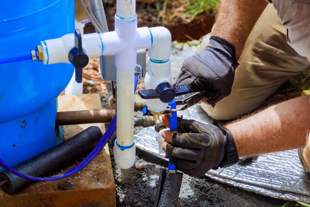 Técnico com luvas instalando registro e tubulação de PVC junto ao tanque azul, instalação do sistema de tratamento