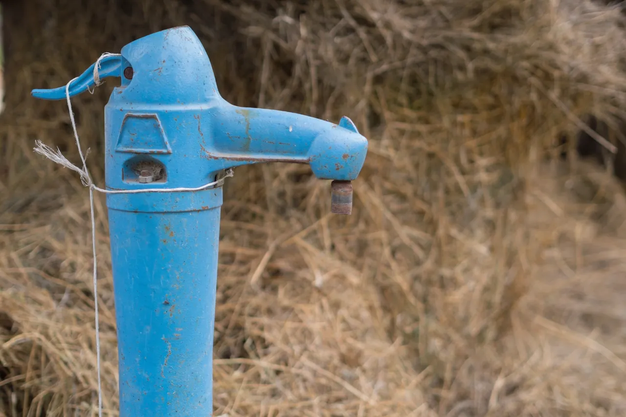 Bomba manual azul de poço sobre palha seca, ponto de captação que passa por limpeza e desinfecção de poço artesiano no RJ
