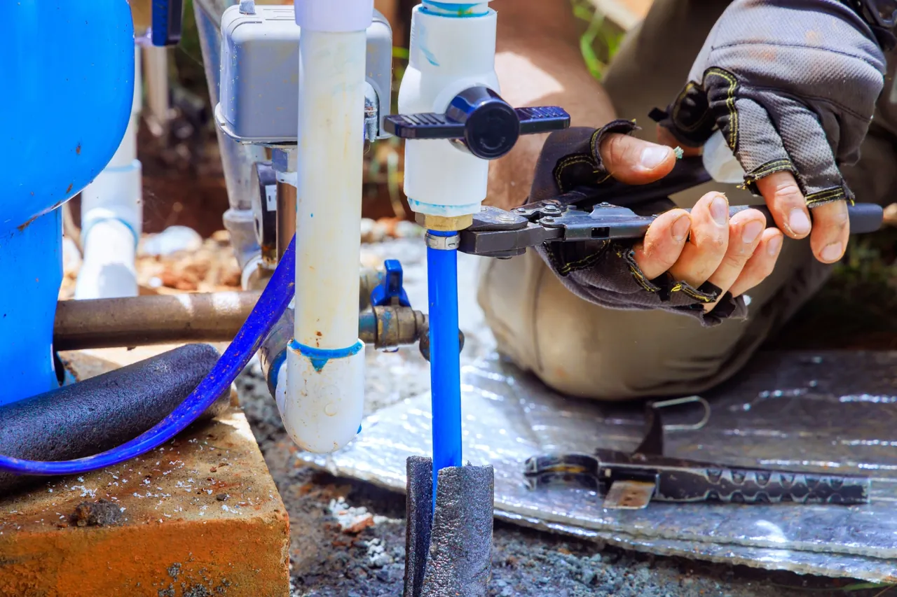 Mãos de técnico com luvas e alicate em tubulação de PVC com isolamento térmico, serviço de manutenção preventiva de poço artesiano no RJ